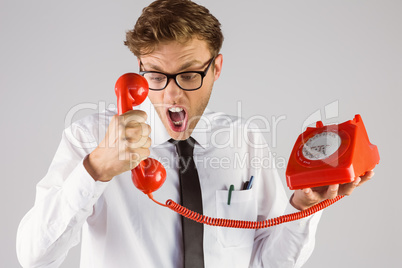 Angry geeky businessman holding telephone