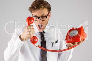 Angry geeky businessman holding telephone