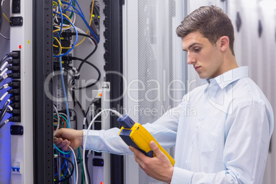 Focused technician using digital cable analyser on servers