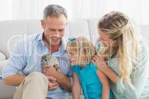 Smiling parents and daughter sitting with rabbit together