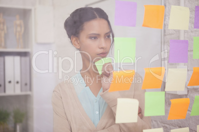 Thoughtful businesswoman looking at sticky notes on window