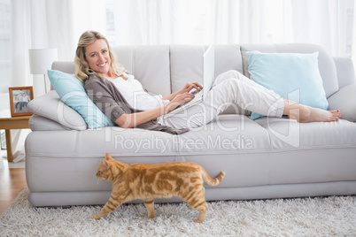 Woman lying on sofa using her laptop smiling at camera