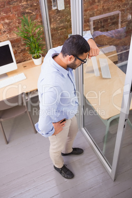 Thoughtful businessman standing against glass wall at office