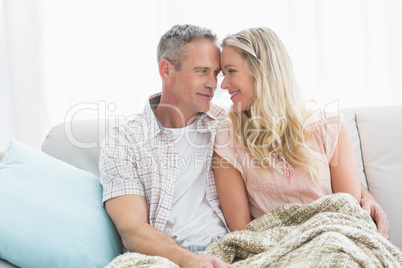 Affectionate couple sitting on sofa under blanket