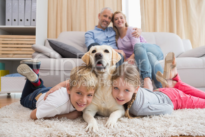 Parents watching children on rug with labrador