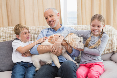 Father with his children on sofa playing with puppy