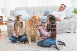 Smiling sisters petting their golden retriever on rug