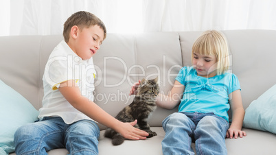 Siblings sitting on the couch stroking their cat