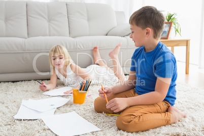 Smiling siblings drawing lying on the floor