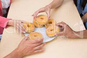 Business team reaching for doughnuts on table