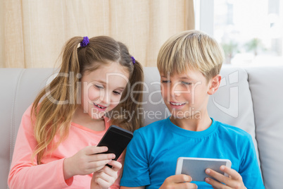 Happy siblings using smartphones on sofa