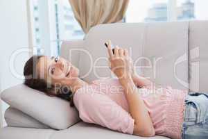 Pretty brunette using smartphone on the couch