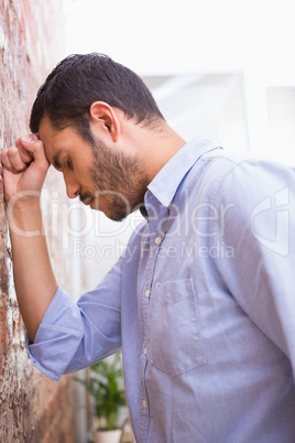 Thoughtful young businessman standing against wall