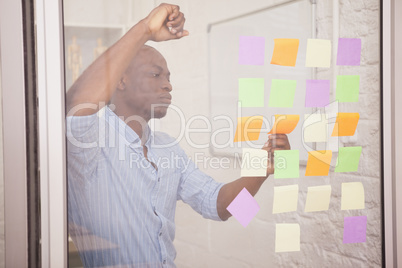 Thoughtful businessman looking at sticky notes on window