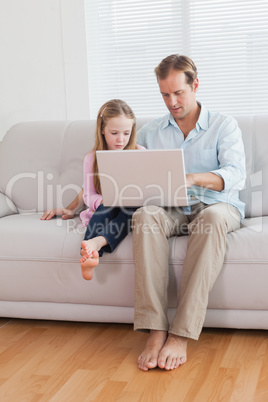 Casual father and daughter using laptop on the couch