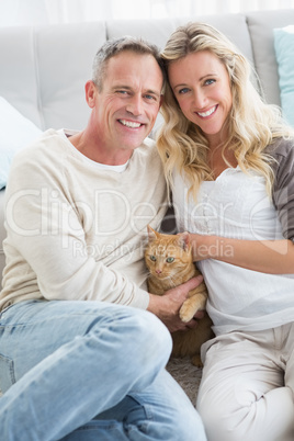 Smiling couple petting their gringer cat on rug