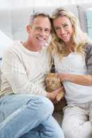 Smiling couple petting their gringer cat on rug