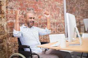 Casual businessman in wheelchair cheering at his desk