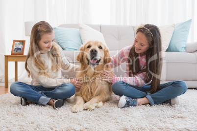 Smiling sisters petting their golden retriever on rug