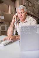 Warehouse manager using telephone and laptop