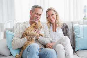 Smiling couple petting their gringer cat on the couch