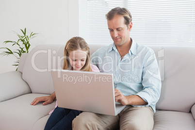 Casual father and daughter using laptop on the couch