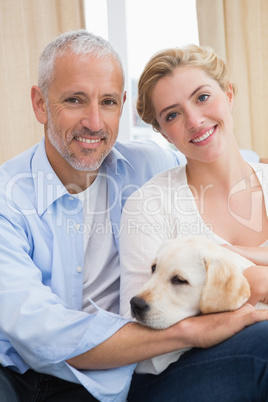 Happy couple cuddling with puppy on sofa