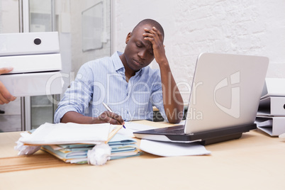 Annoyed businessman taking notes while holding his head