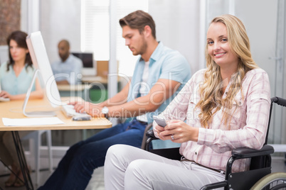 Woman in wheelchair texting on phone and smiling at camera