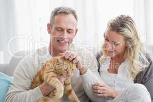 Smiling couple petting their gringer cat on the couch