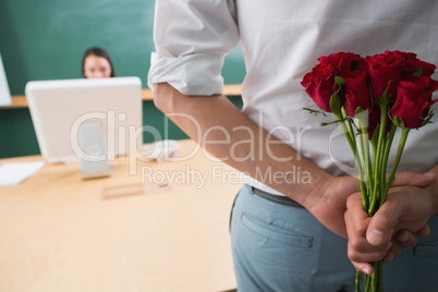 Man hiding bouquet in front of businesswoman at desk