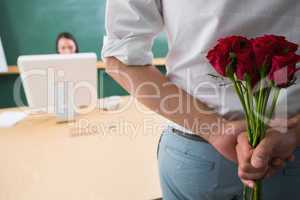 Man hiding bouquet in front of businesswoman at desk