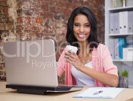 Smiling woman with coffee cup and laptop sitting at her desk