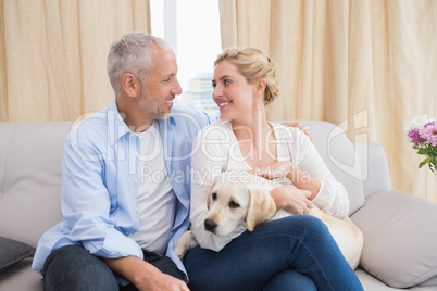 Happy couple cuddling with puppy on sofa