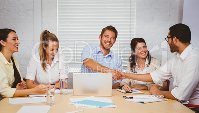 Casual business people shaking hands at desk and smiling Casual business people shaking hands at desk and smiling