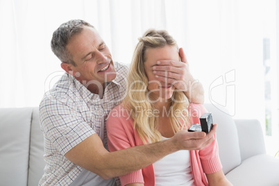 Man covering partner eyes and offering a gift to her