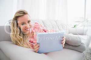 Blonde woman lying on her couch using her digital tablet