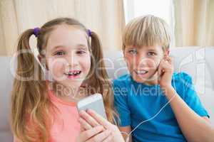 Happy siblings listening to music on sofa