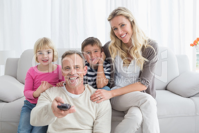 Smiling family sitting on sofa changing tv channel