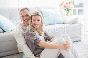 Happy casual couple sitting on rug smiling at camera