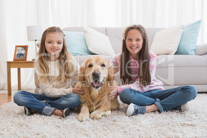 Smiling sisters petting their golden retriever on rug