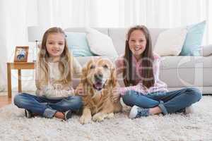 Smiling sisters petting their golden retriever on rug