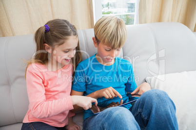 Happy siblings using tablet pc on sofa