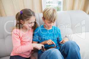 Happy siblings using tablet pc on sofa