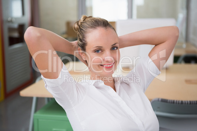 Smiling businesswoman with hands behind head in office