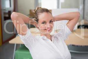 Smiling businesswoman with hands behind head in office