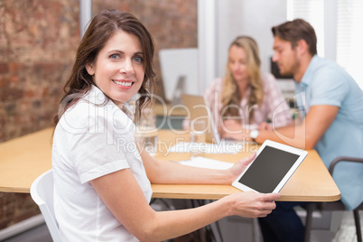 Woman on tablet smiling at camera with colleagues behind