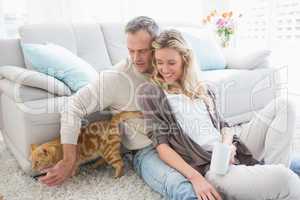 Cute couple sitting having coffee and petting their cat
