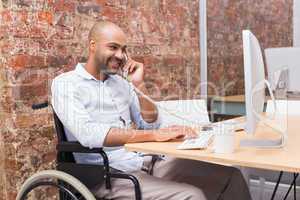 Businessman in wheelchair working at his desk on the phone