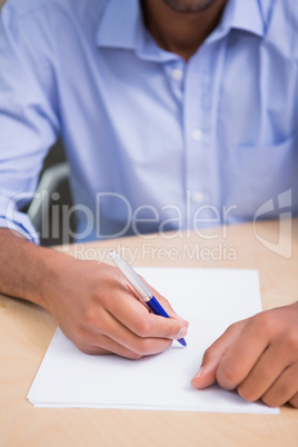 Mid section of businessman writing document at desk